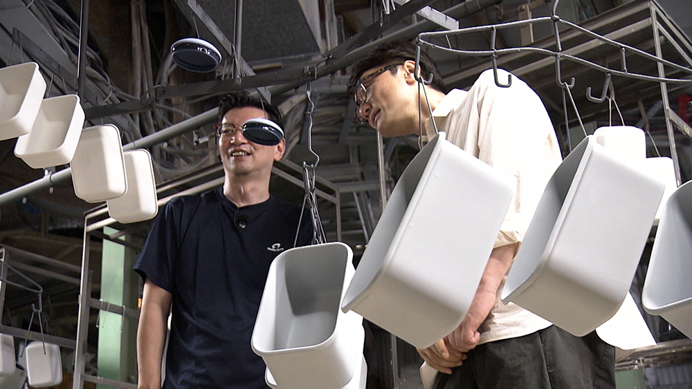 Kikuchi watches enamelware proceed along the production line